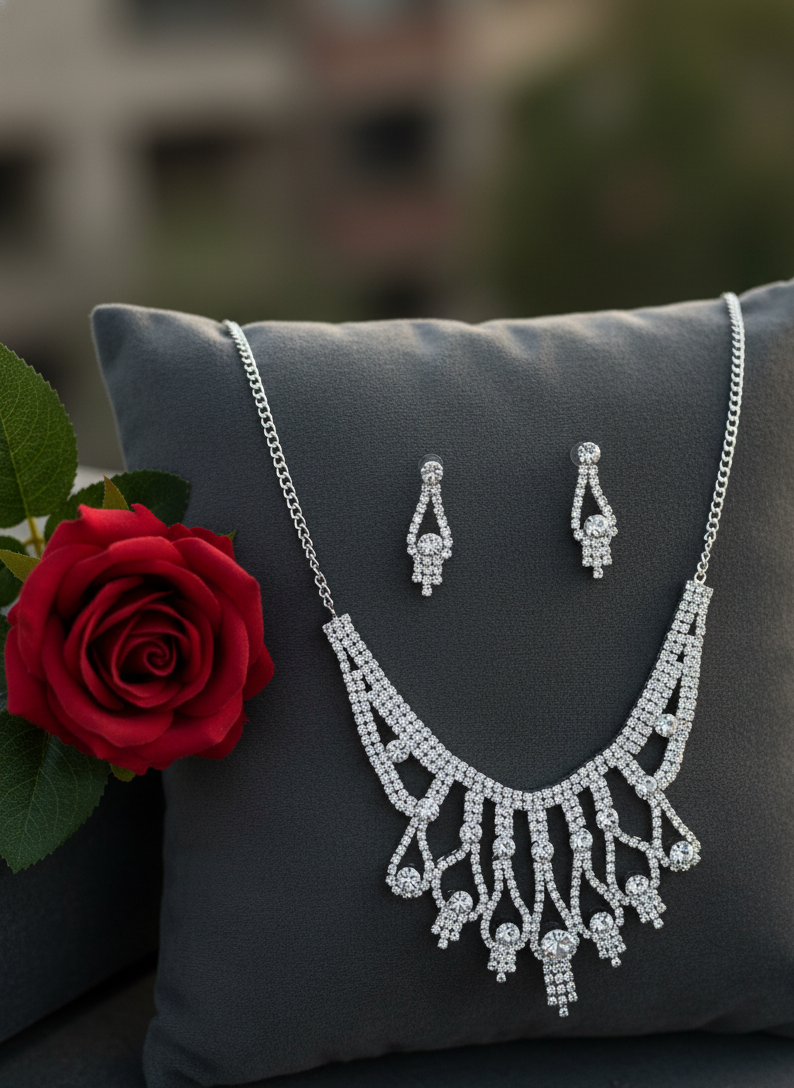 Silver necklace and earrings set on a gray pillow with a red rose.