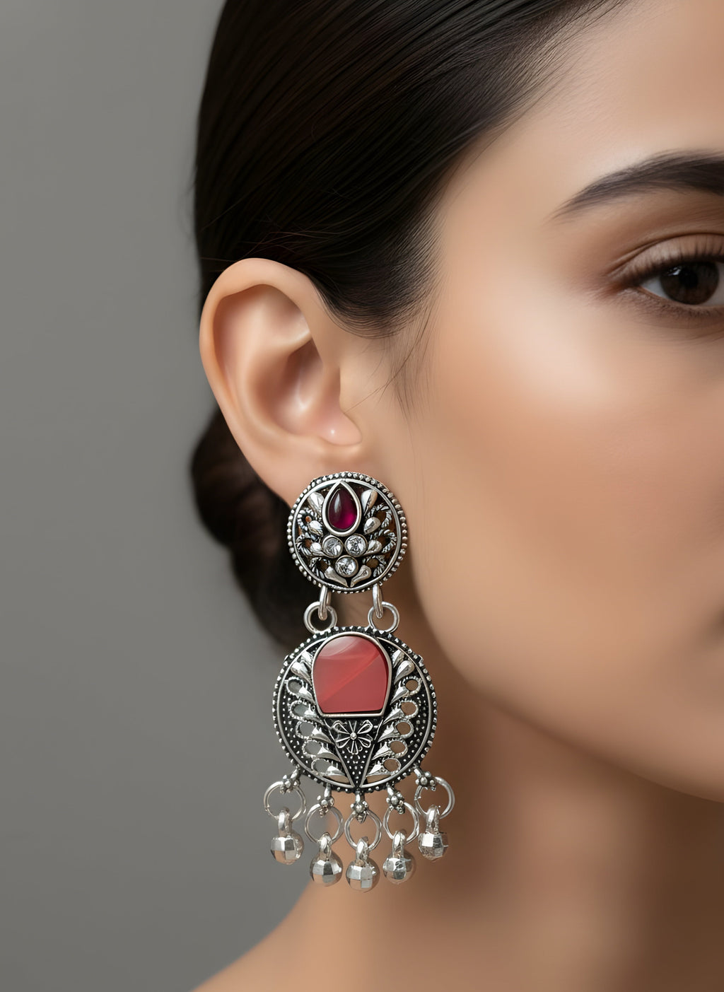 Close-up of a woman wearing a decorative earring with red stones and silver details on a neutral background.