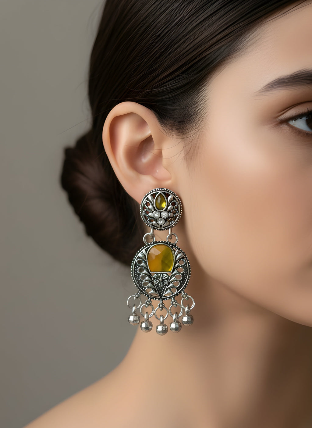 Close-up of a woman wearing a silver earring with a yellow gemstone against a neutral background