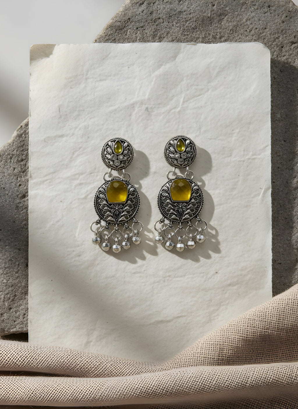 Pair of silver earrings with yellow gemstones on a white stone surface