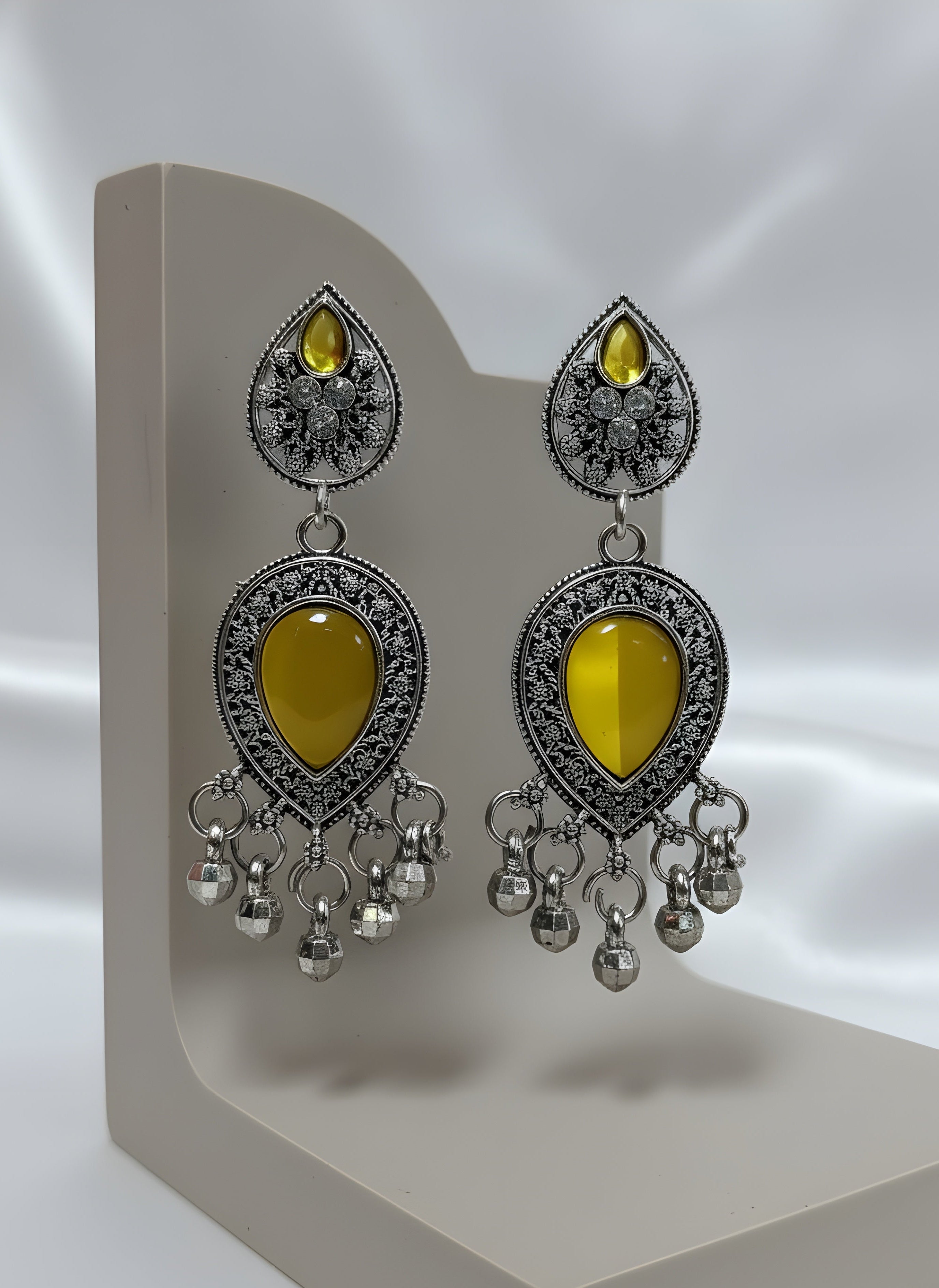 Pair of earrings with yellow teardrop stones and silver accents on a gray stand.
