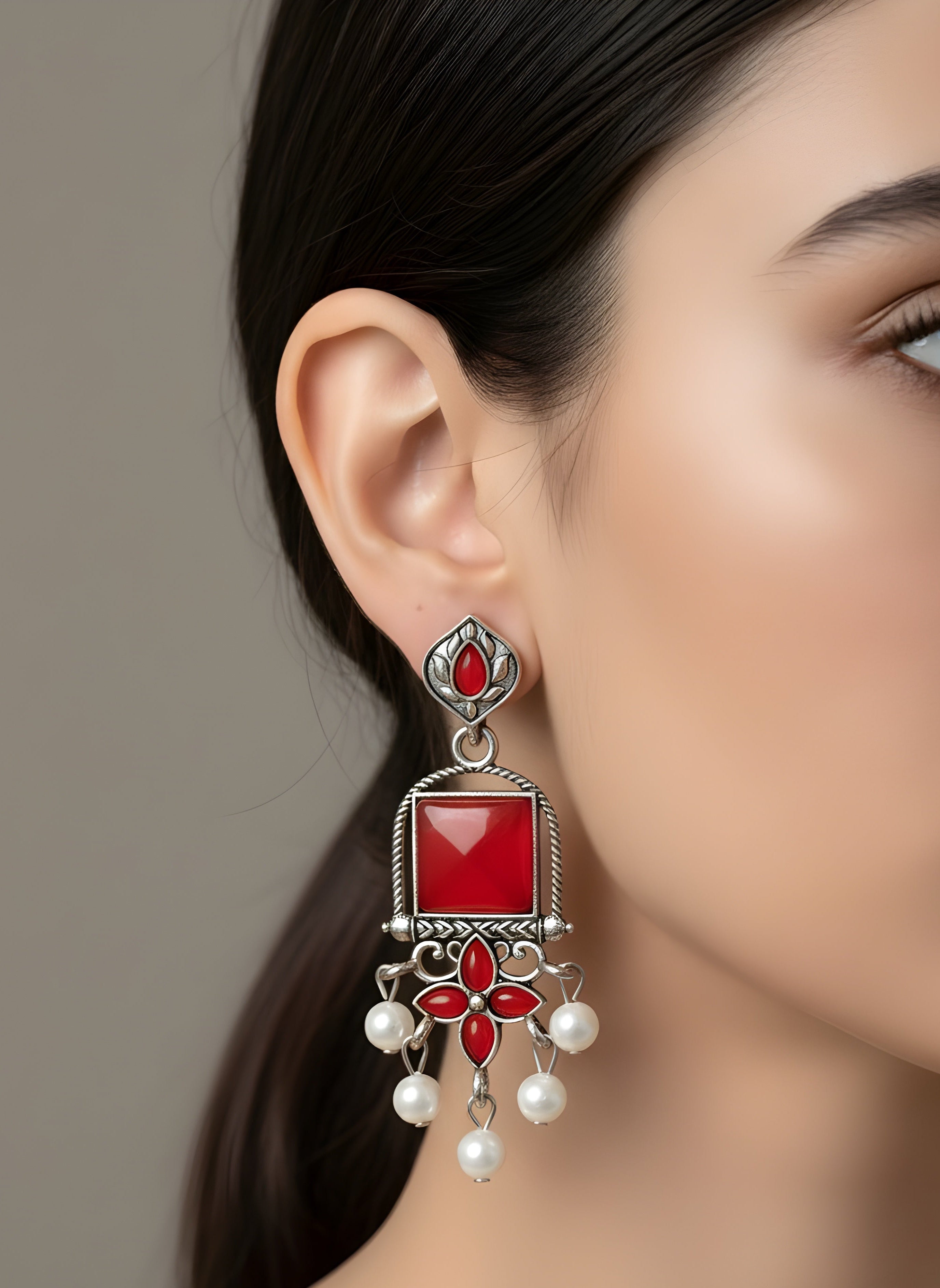Close-up of a woman wearing a red gemstone earring with silver and pearl details.