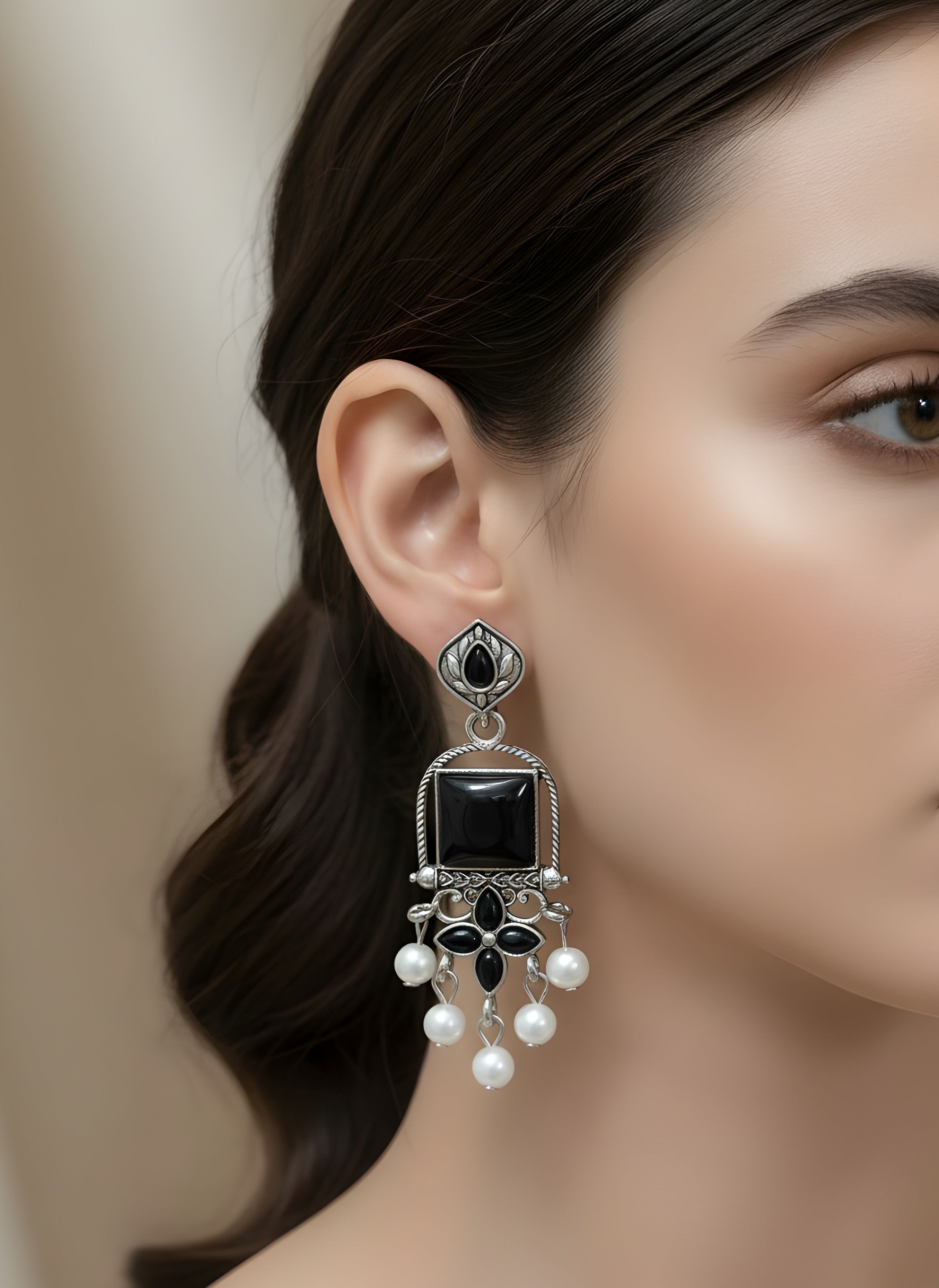 Close-up of a woman wearing an elegant earring with a black gemstone and pearl accents.