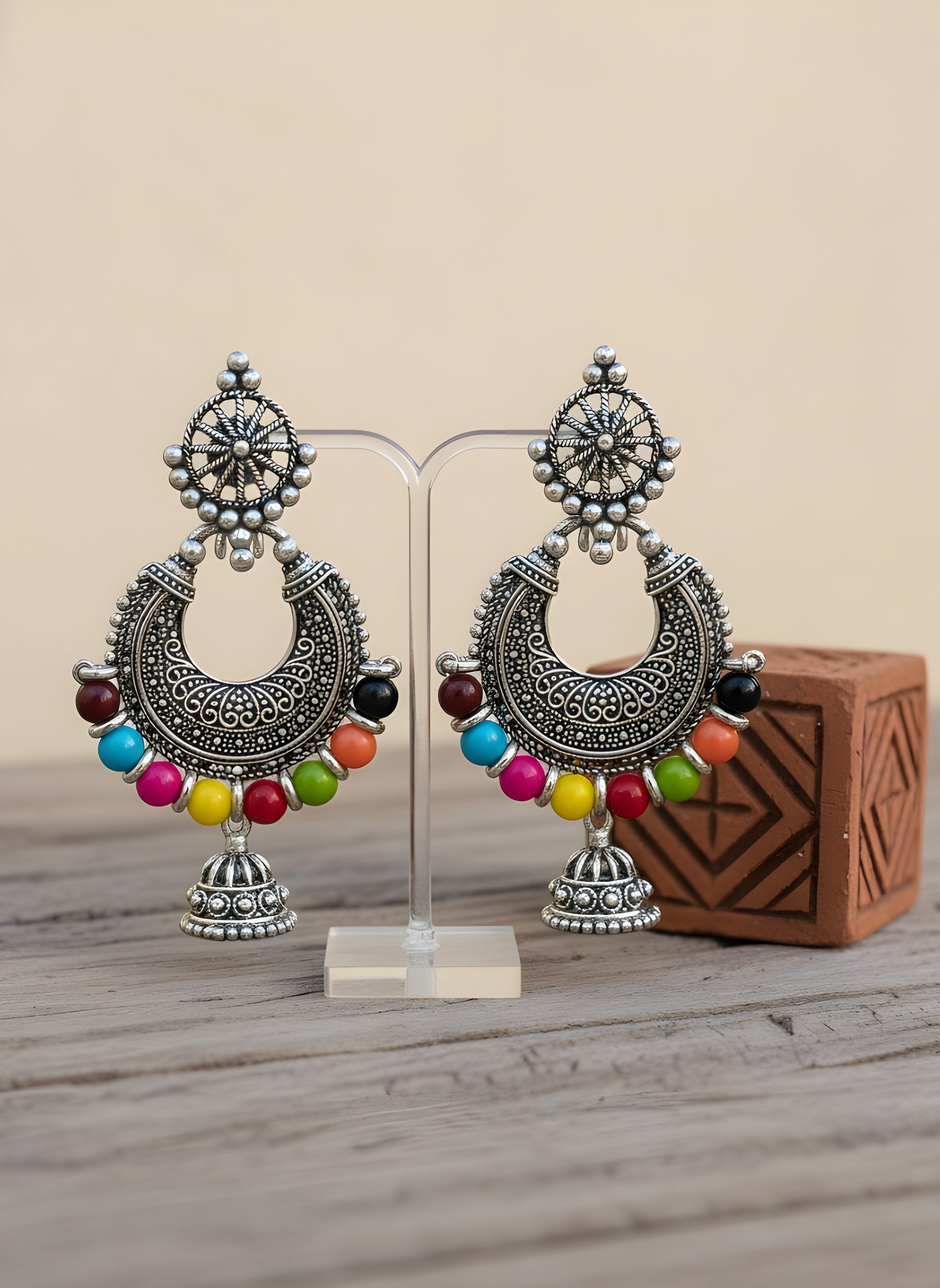 Ornate silver earrings with colorful beads on a wooden surface
