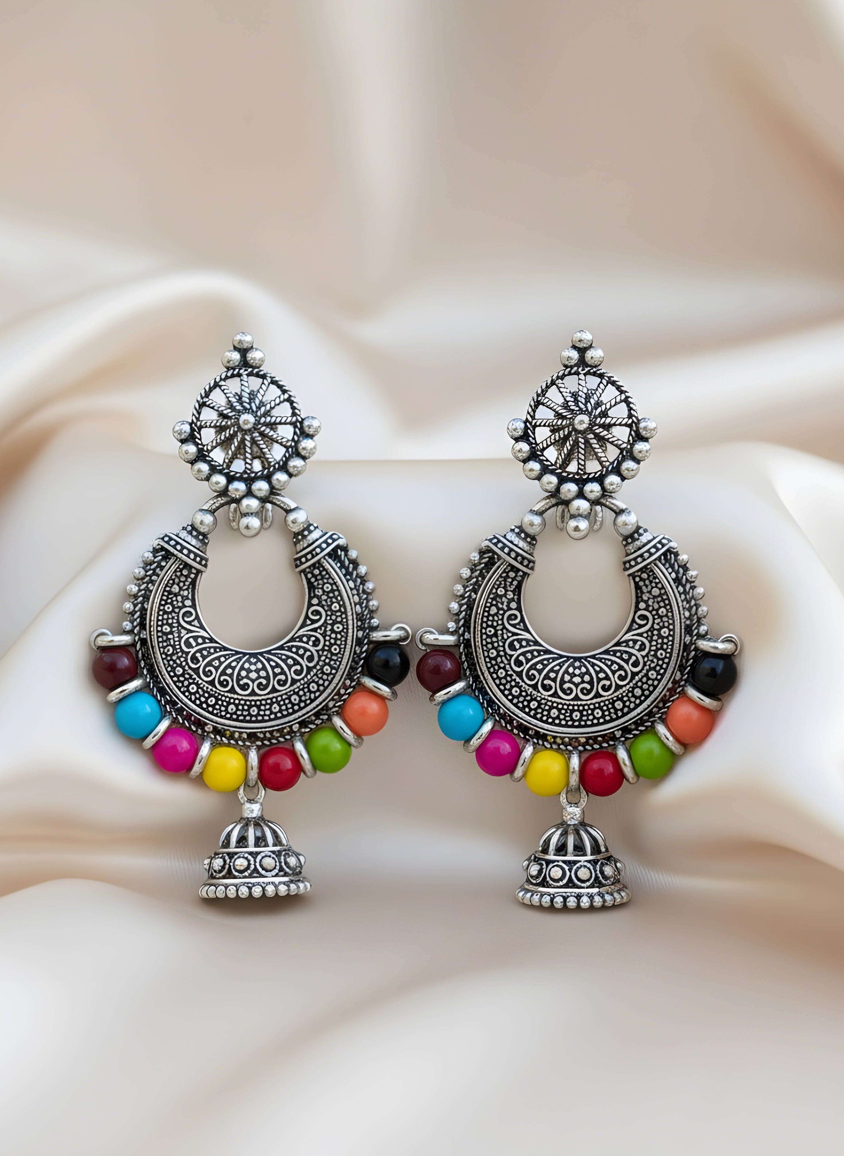 Pair of ornate earrings with colorful beads on a soft fabric background