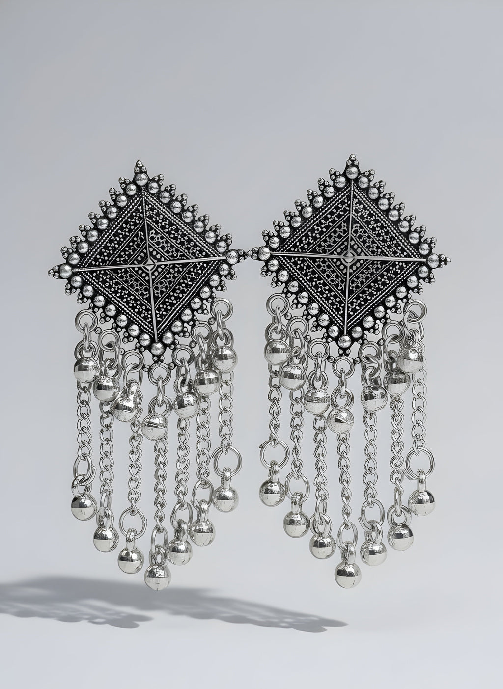 Pair of silver earrings with geometric designs and dangling chains on a white background