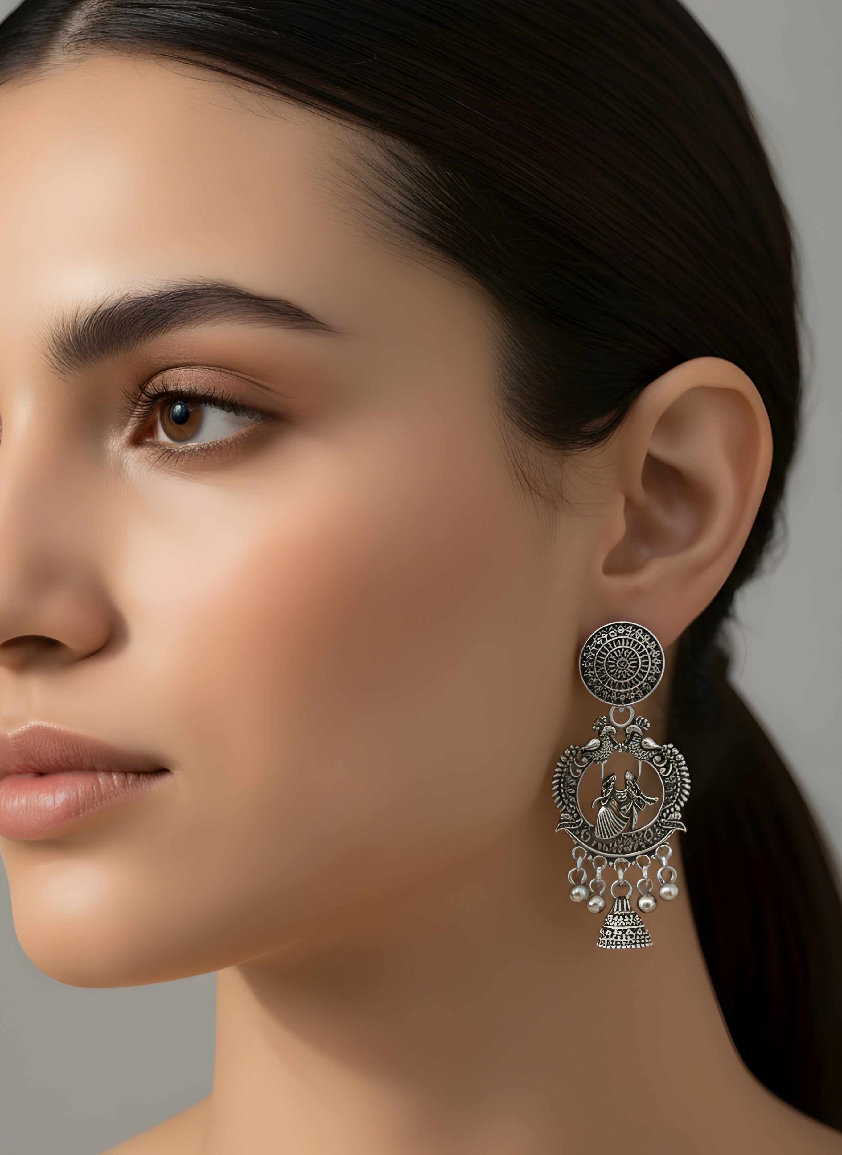 Close-up of a woman wearing a silver earring with intricate design on a neutral background