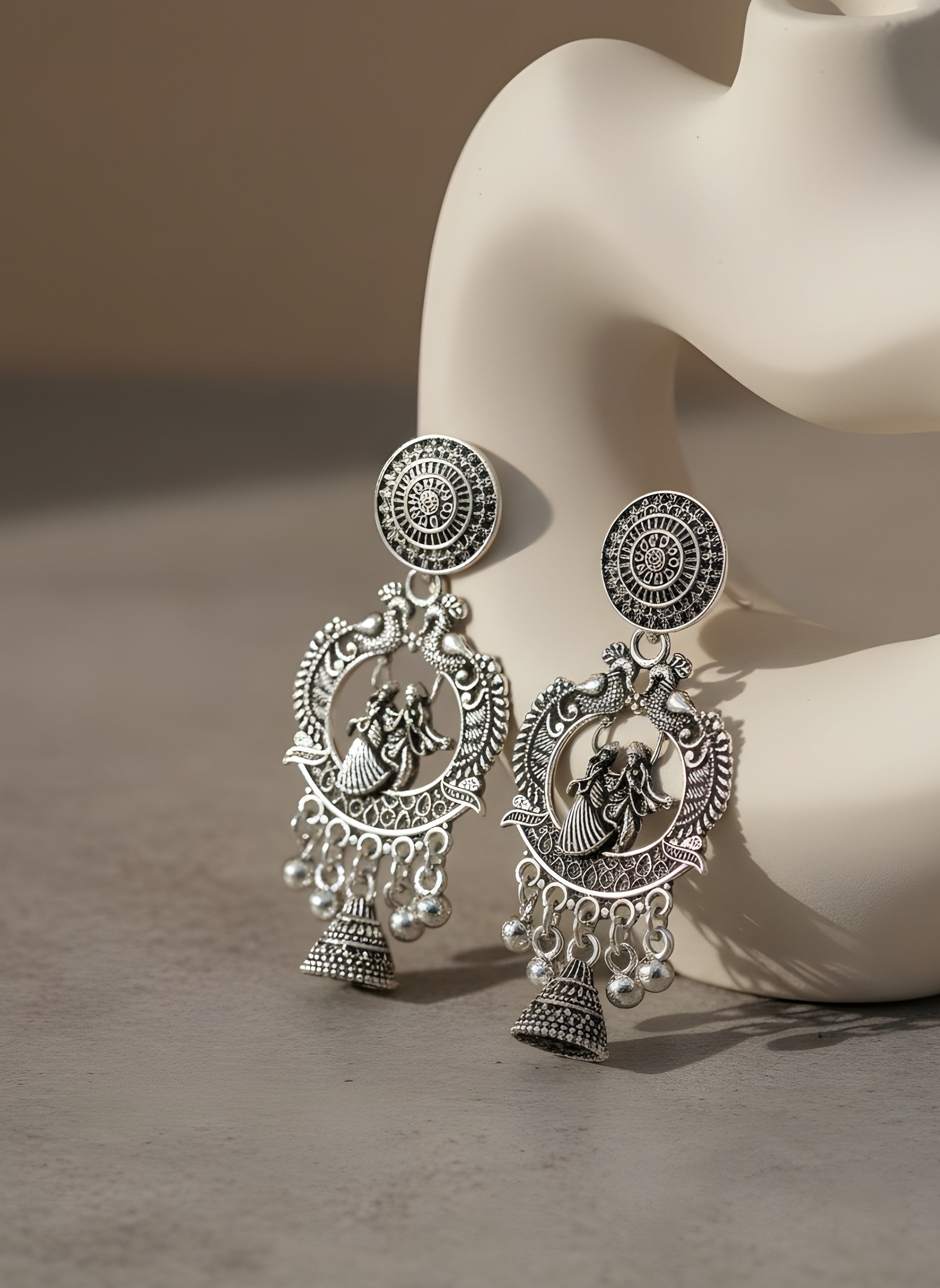 Silver earrings with intricate designs on a mannequin bust against a neutral background
