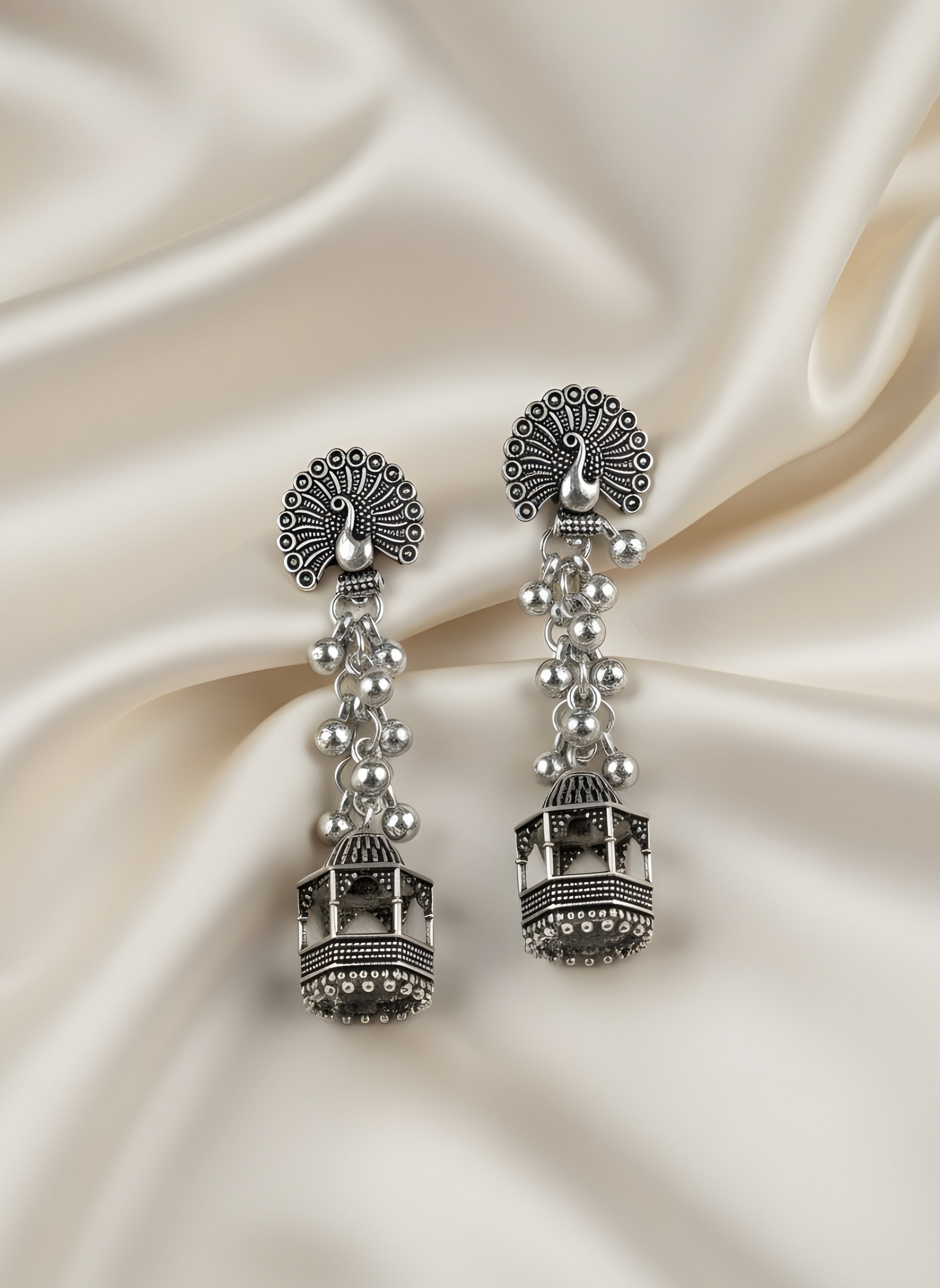 Silver earrings with intricate designs on a satin background