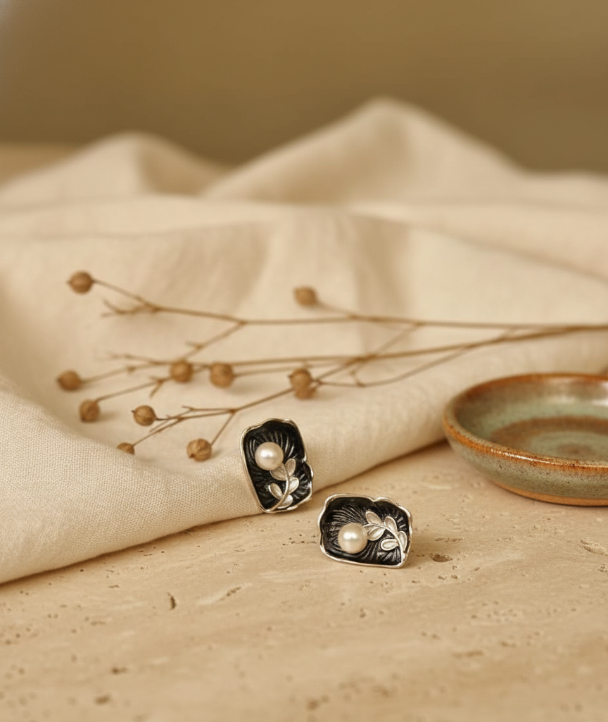 Pair of silver earrings with pearl-like stones on a beige fabric background