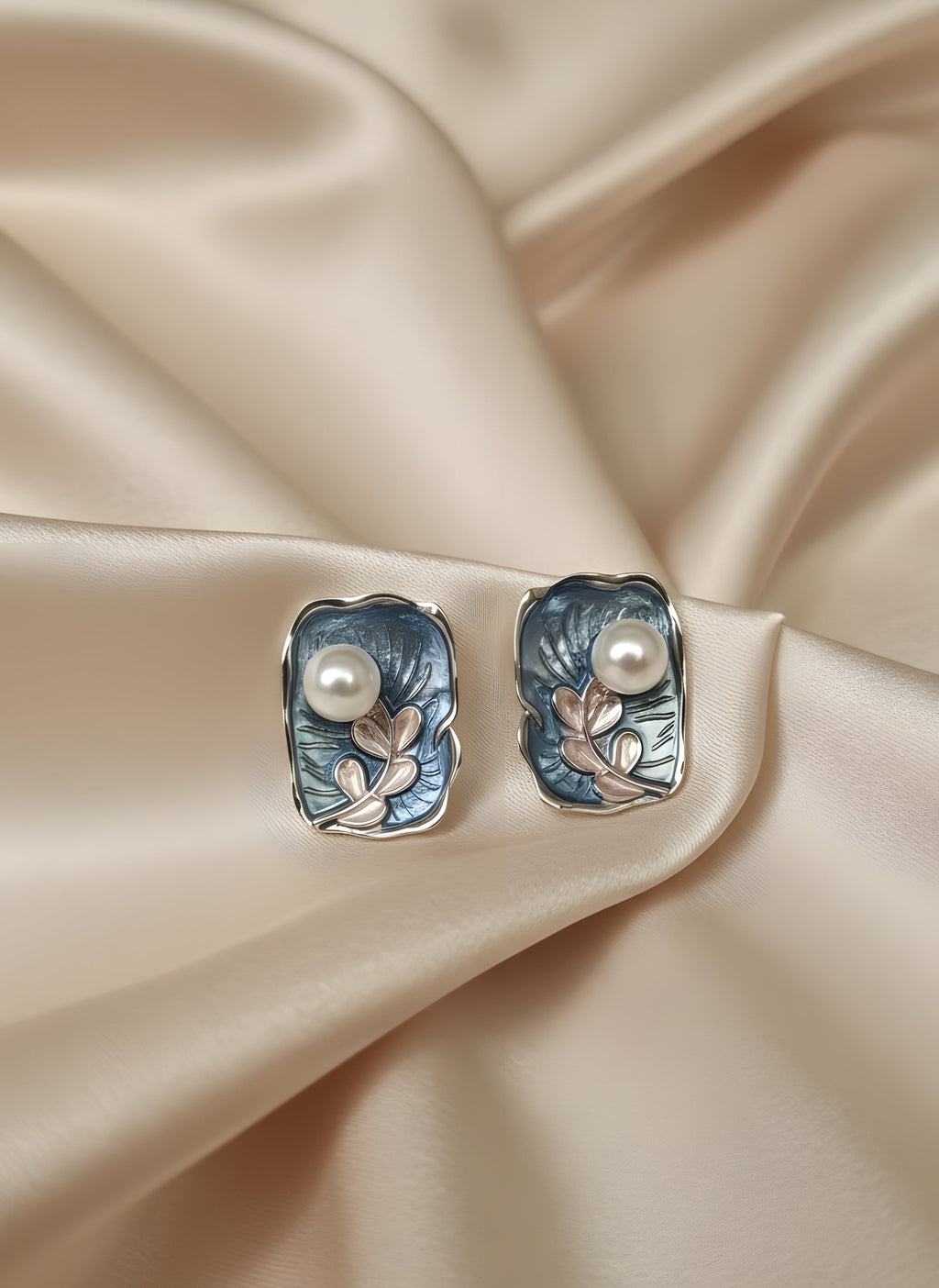 Silver earrings with pearl accents on a beige satin background