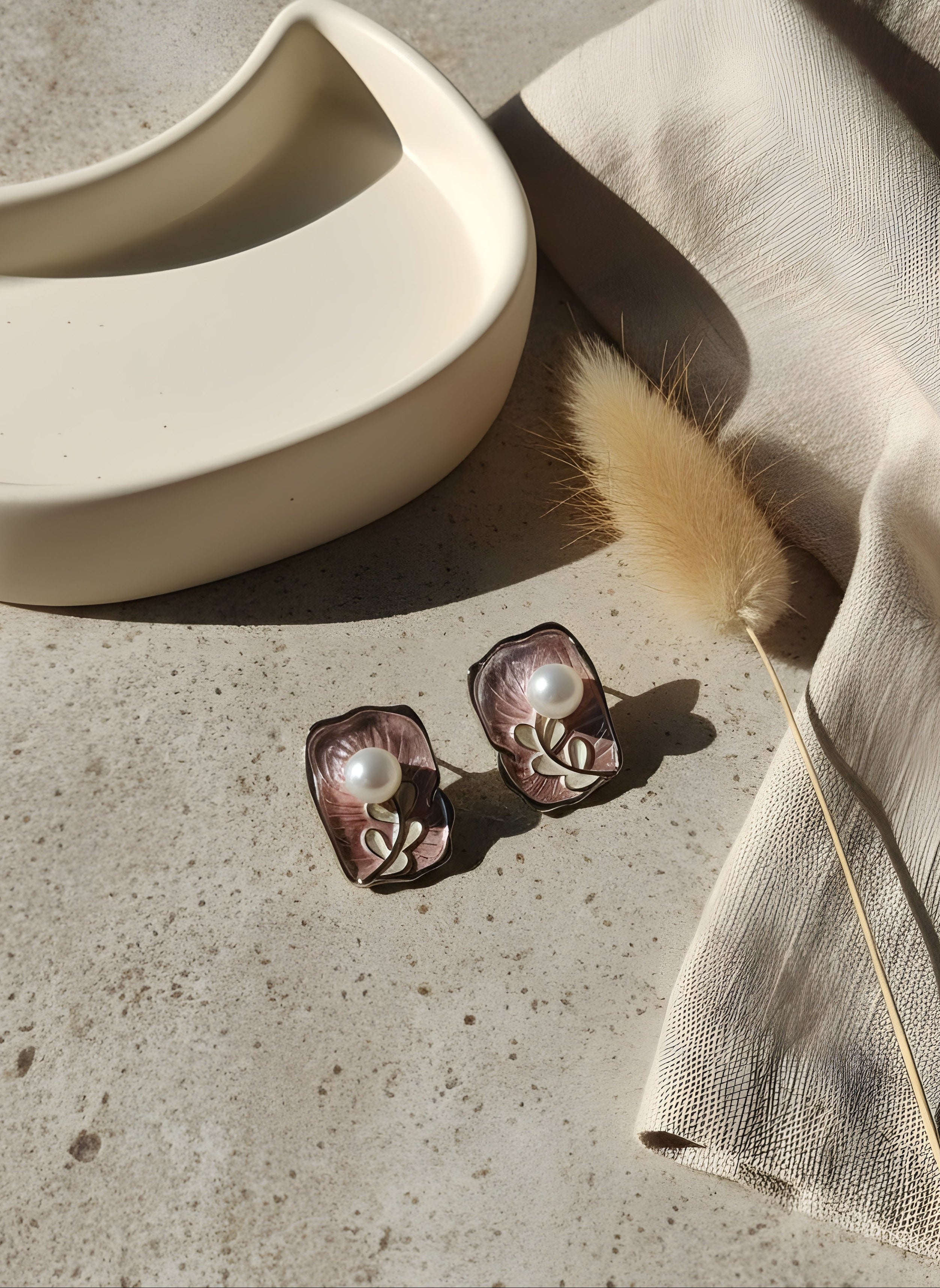 Pair of earrings on a textured surface with a decorative feather and bowl.