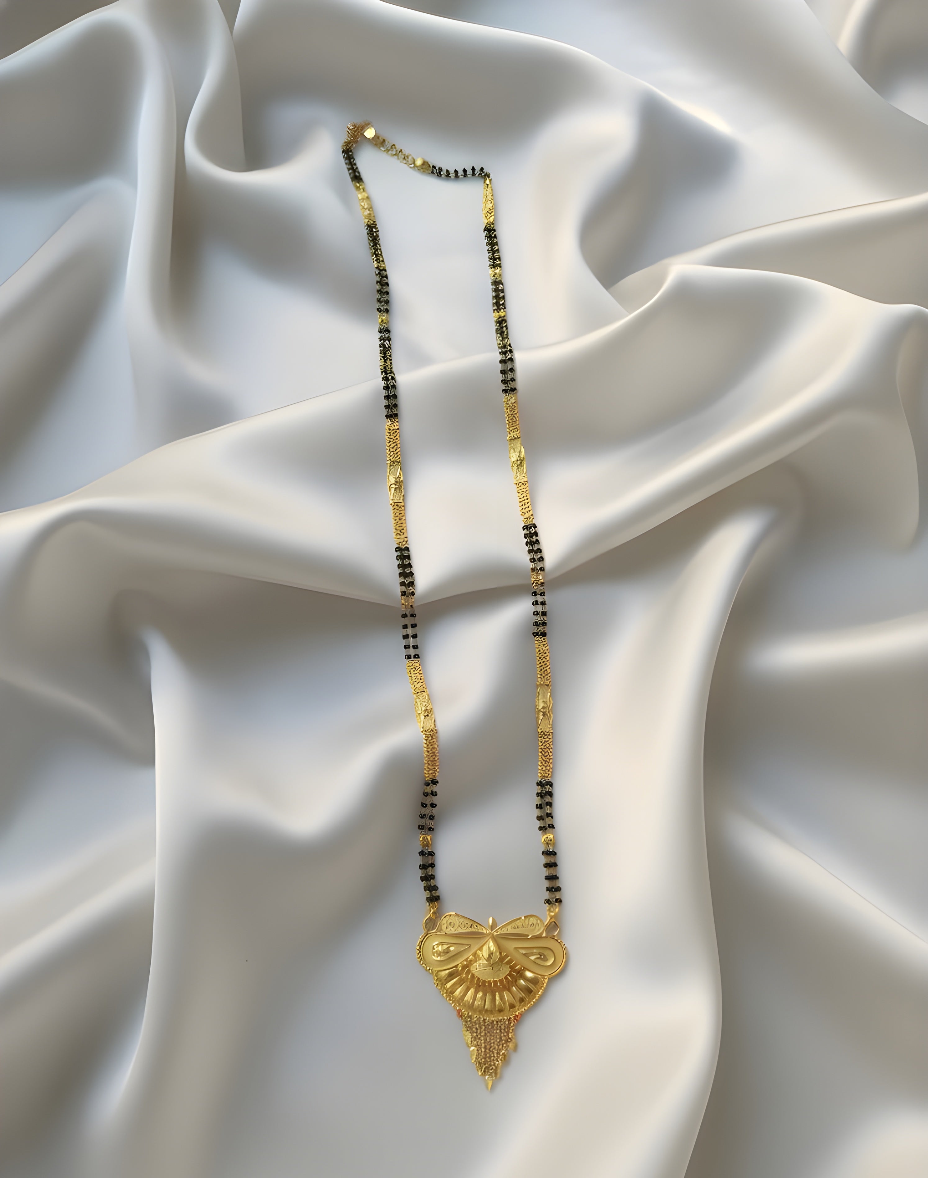 Gold necklace with black beads on a white fabric background