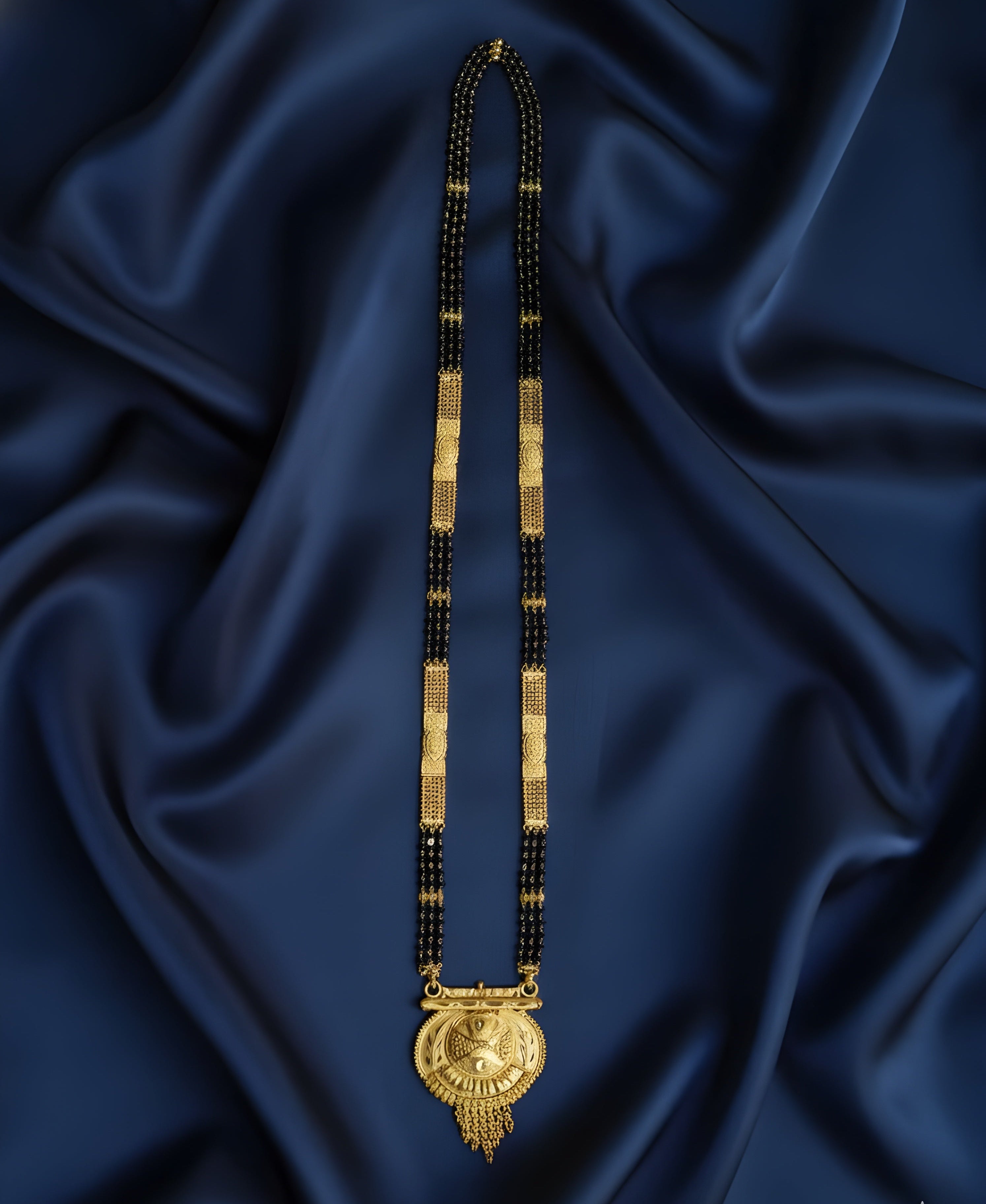 Gold and black beaded necklace with a large pendant on a blue satin background