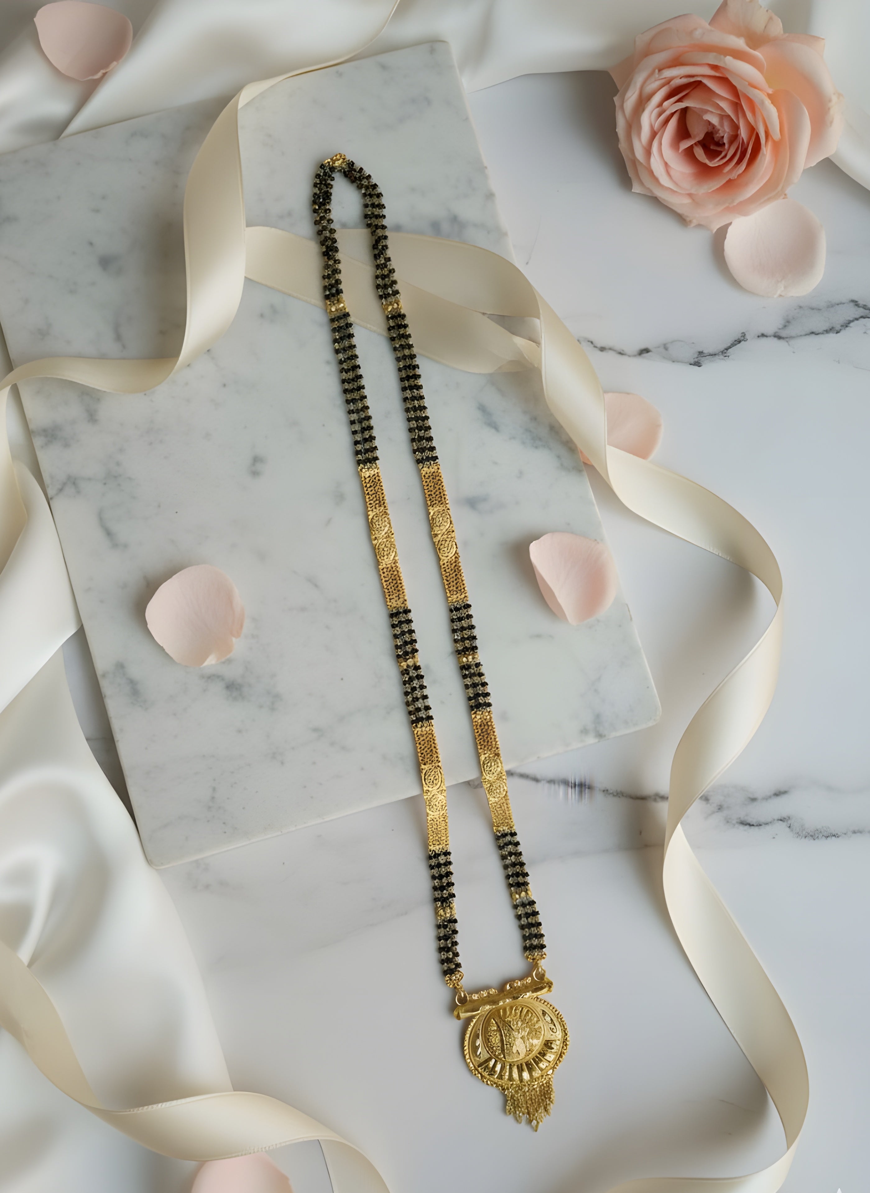 Gold necklace with black beads on a marble surface with pink flowers