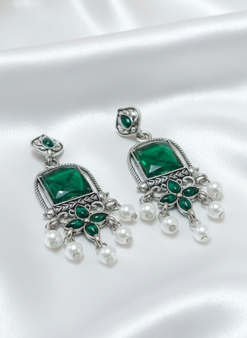 Pair of green gemstone and pearl earrings on a white background