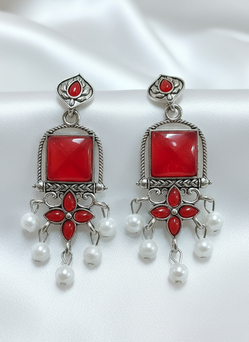 Pair of earrings with red stones and pearl-like beads on a white background