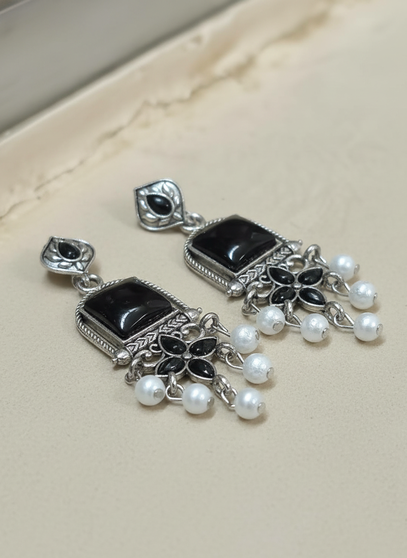 Pair of silver earrings with black stones and pearl-like beads on a beige background