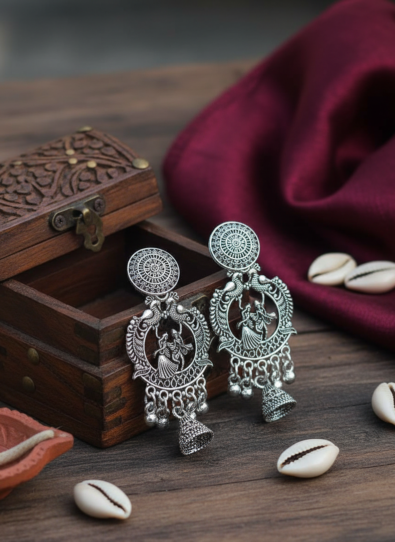 Silver earrings on a wooden surface with a wooden box and cowrie shells.