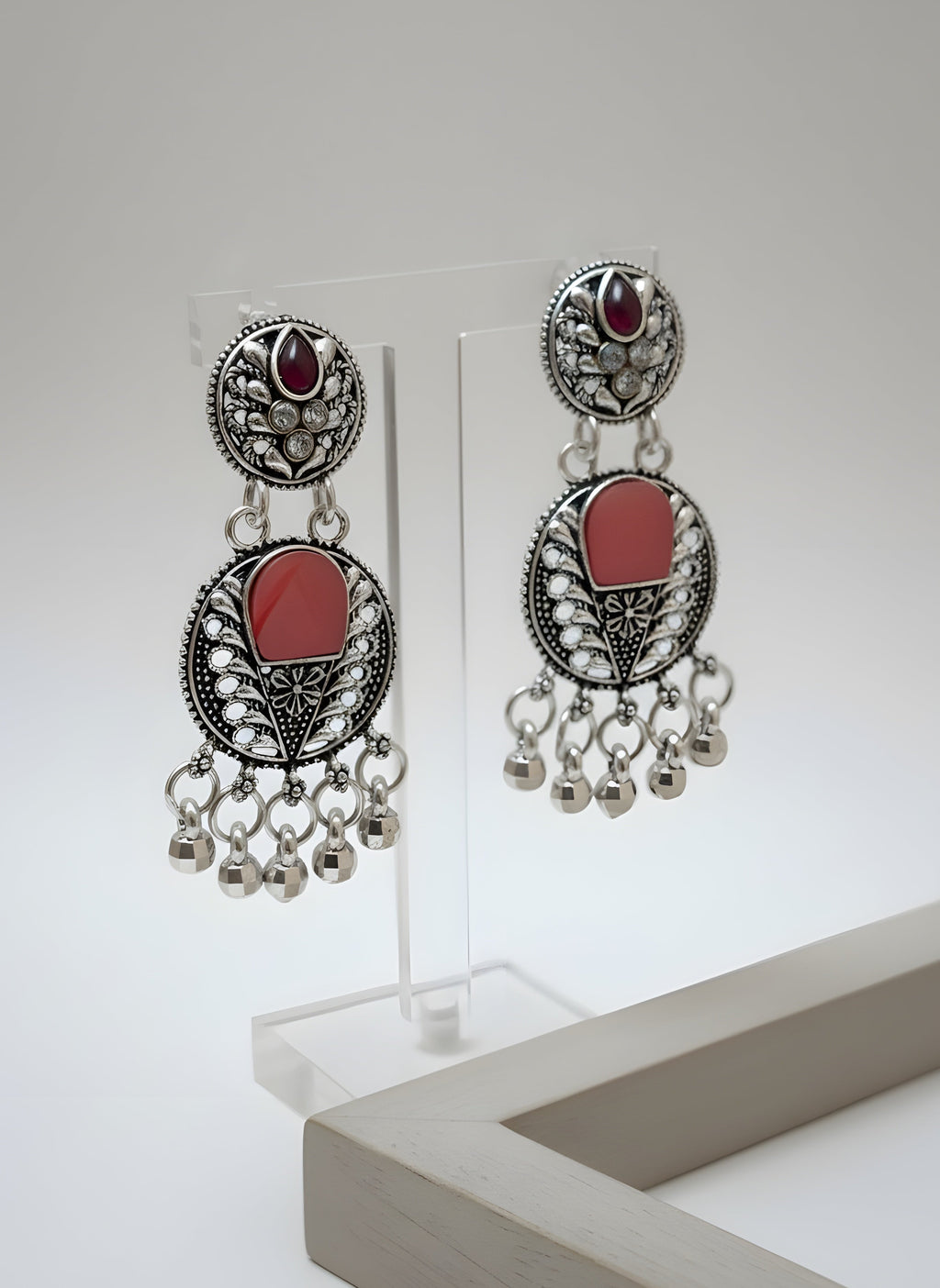 Pair of ornate earrings with red stones and dangling beads on a white background