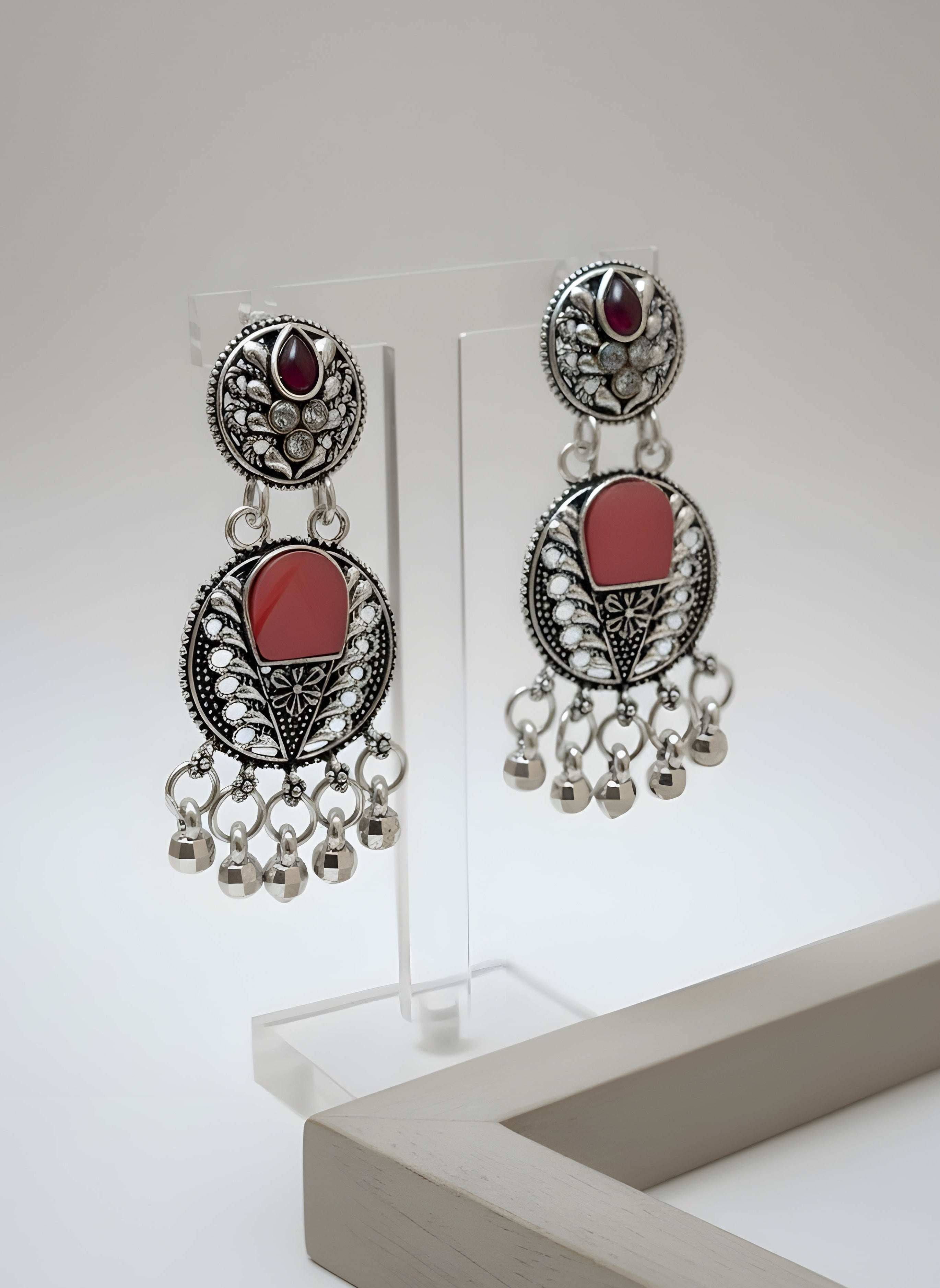 Pair of ornate earrings with red stones and dangling beads on a white background