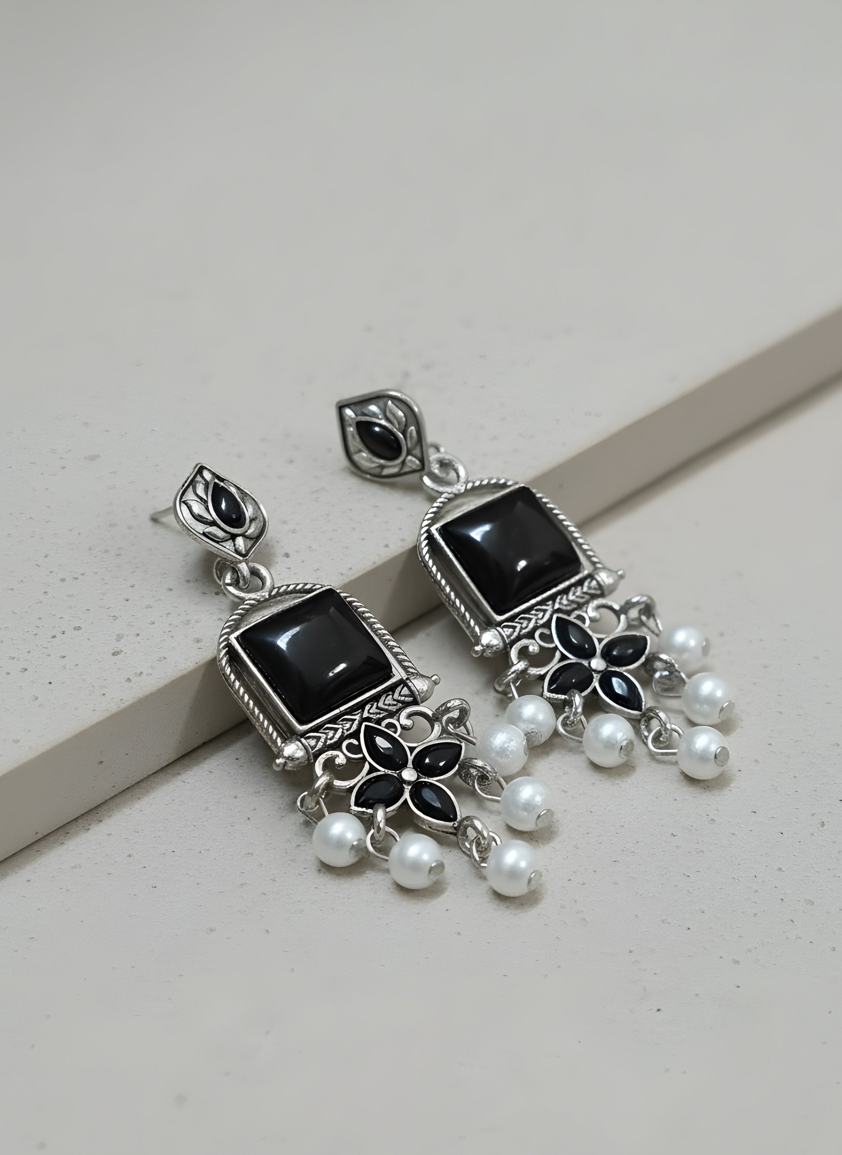 Pair of silver earrings with black stones and pearl-like beads on a light gray background