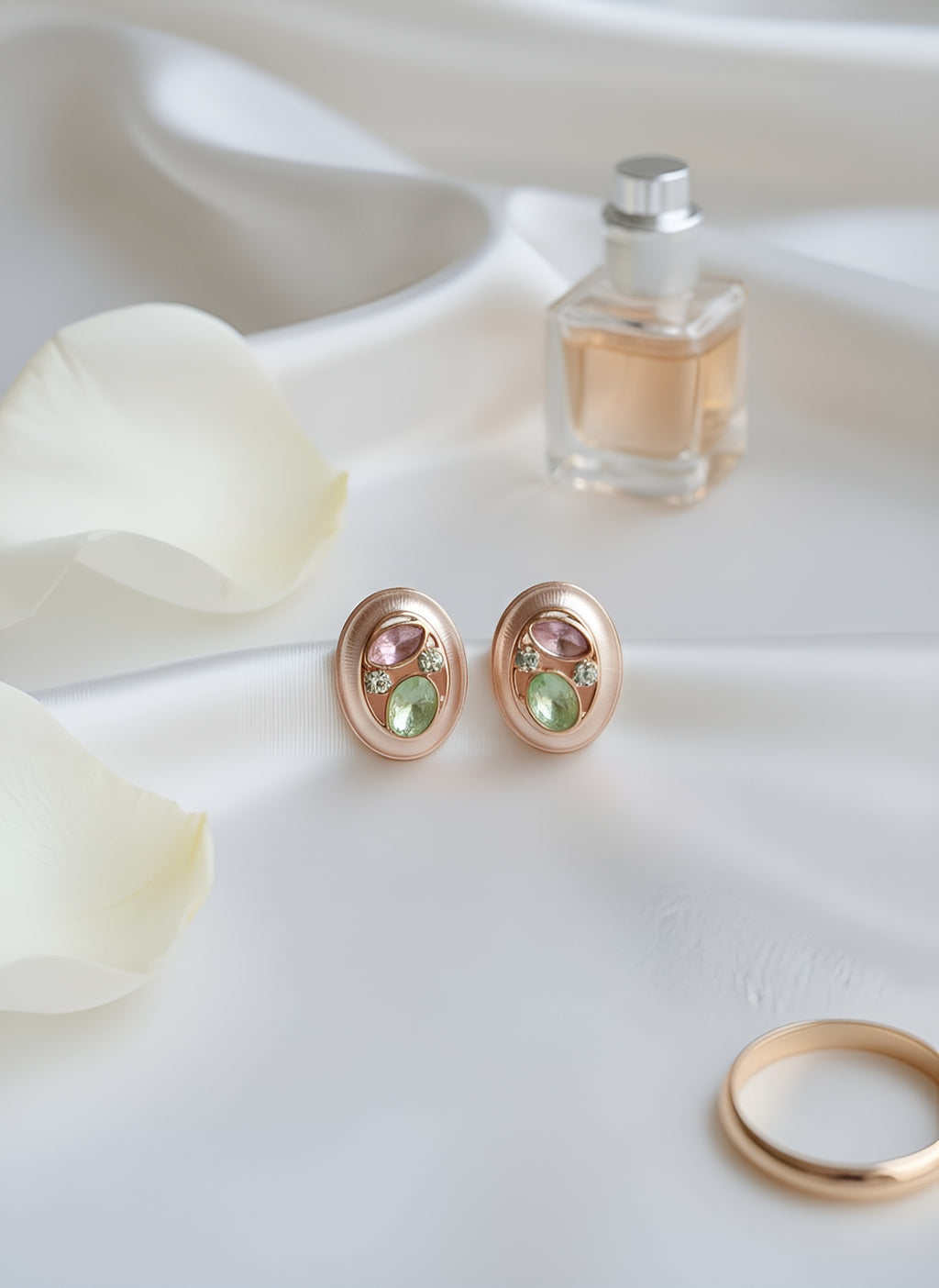 Pair of earrings with gemstones, a ring, and a small bottle of perfume on a white surface.
