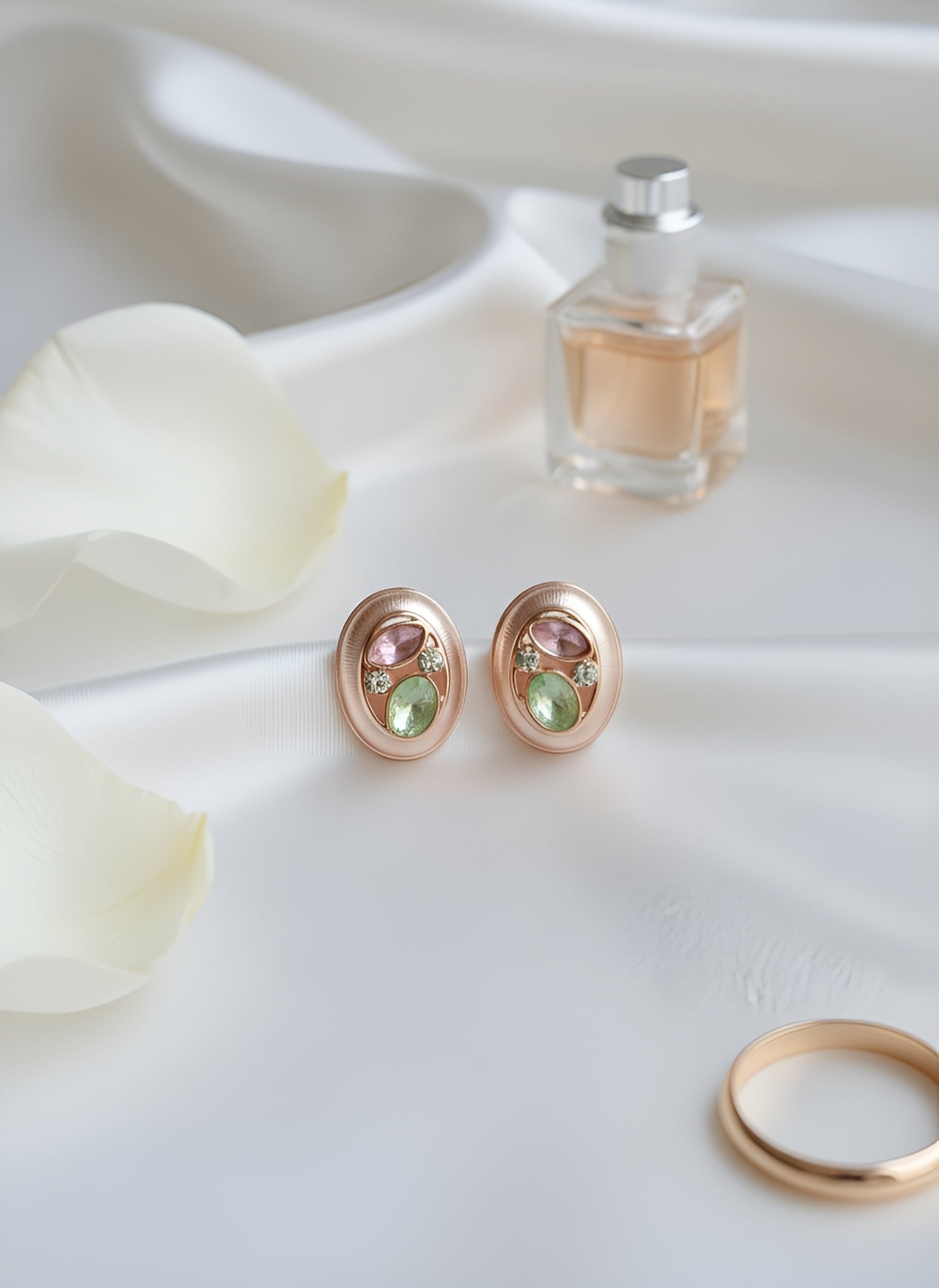 Pair of earrings with gemstones, a ring, and a small bottle of perfume on a white surface.