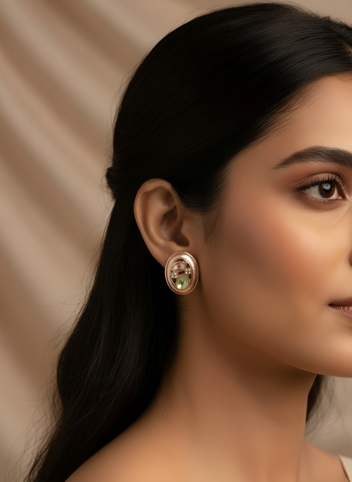 Close-up of a woman wearing a gold earring with a green gemstone against a beige background